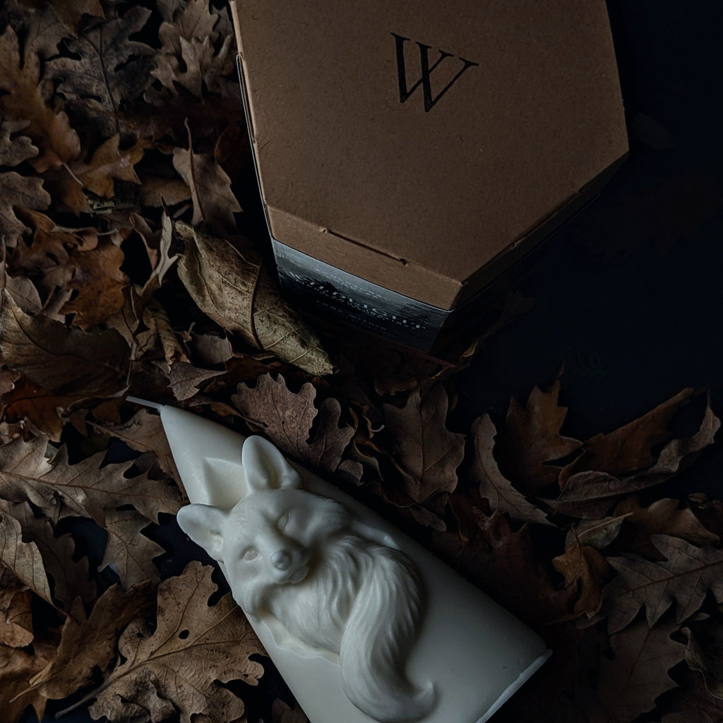 White sculptural fox candle on a dark surface with dried leaves
