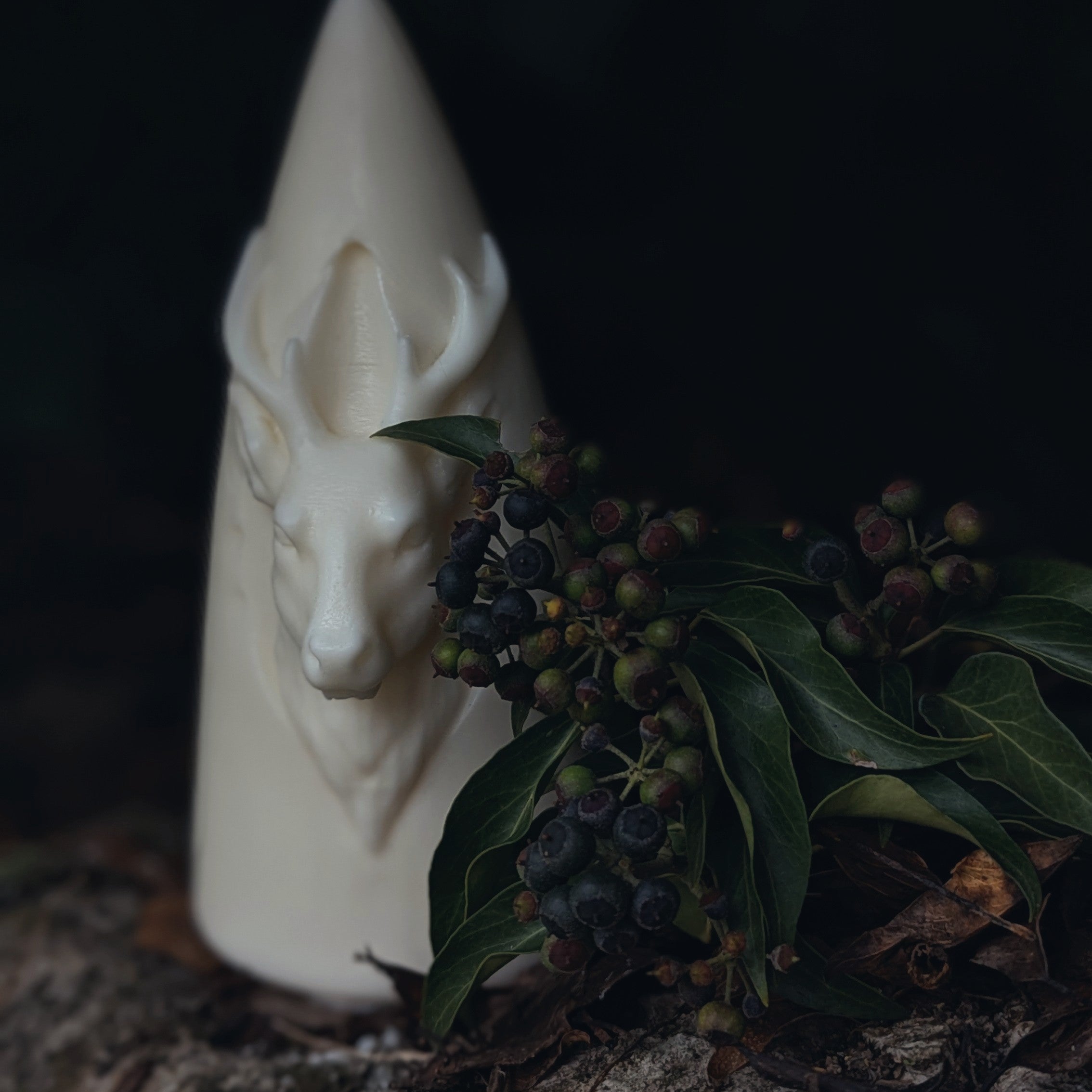White candle with a deer head design on a dark background