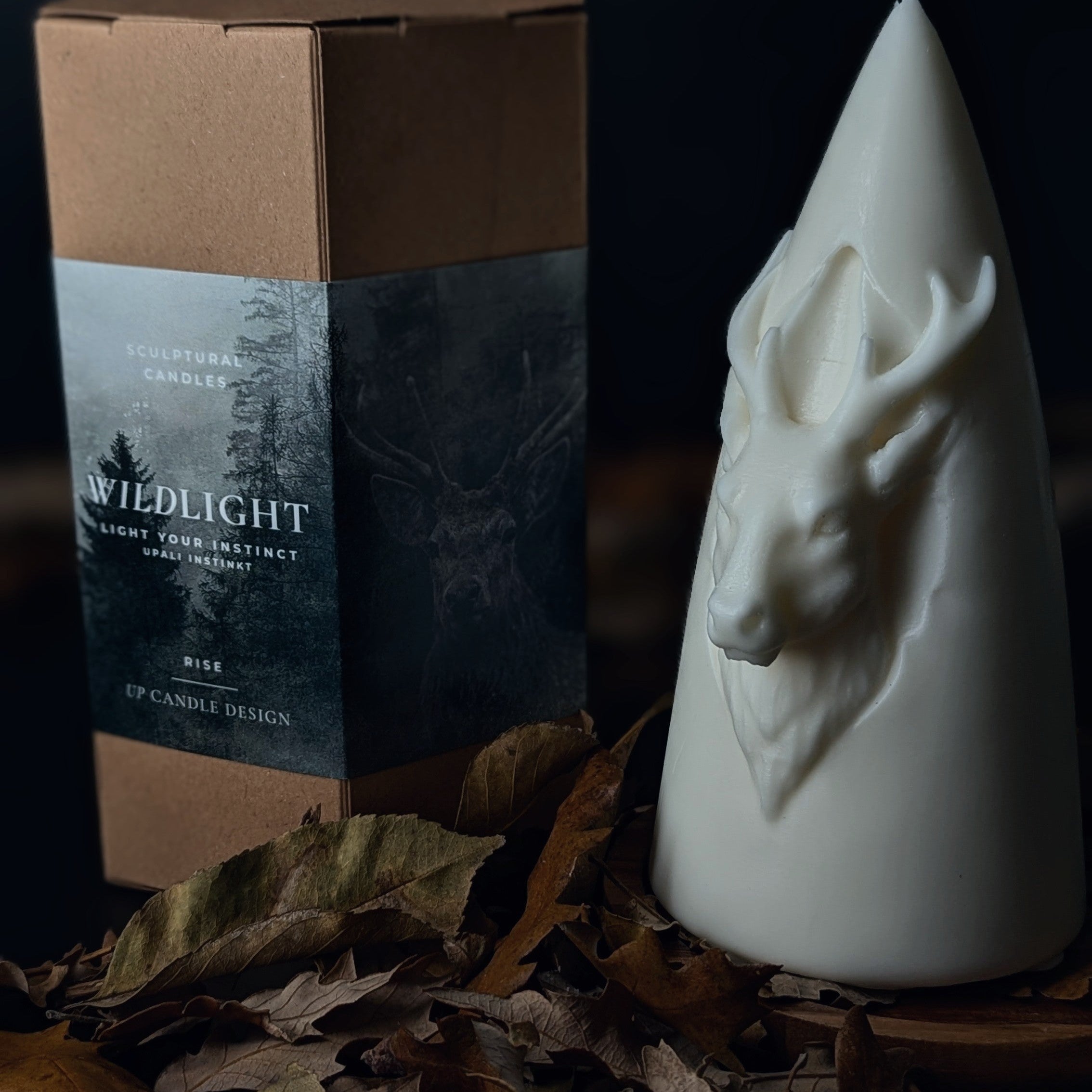 White candle with deer head design next to a box labeled 'Wildlight' on a dark background